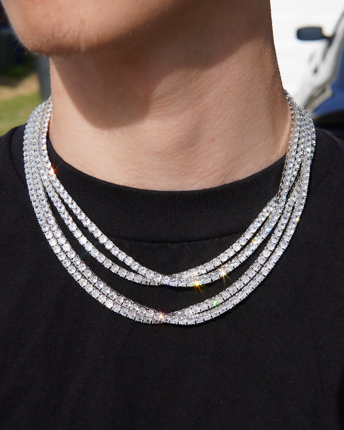 Close-up of a person wearing a multiple-layered diamond necklace on a black shirt.