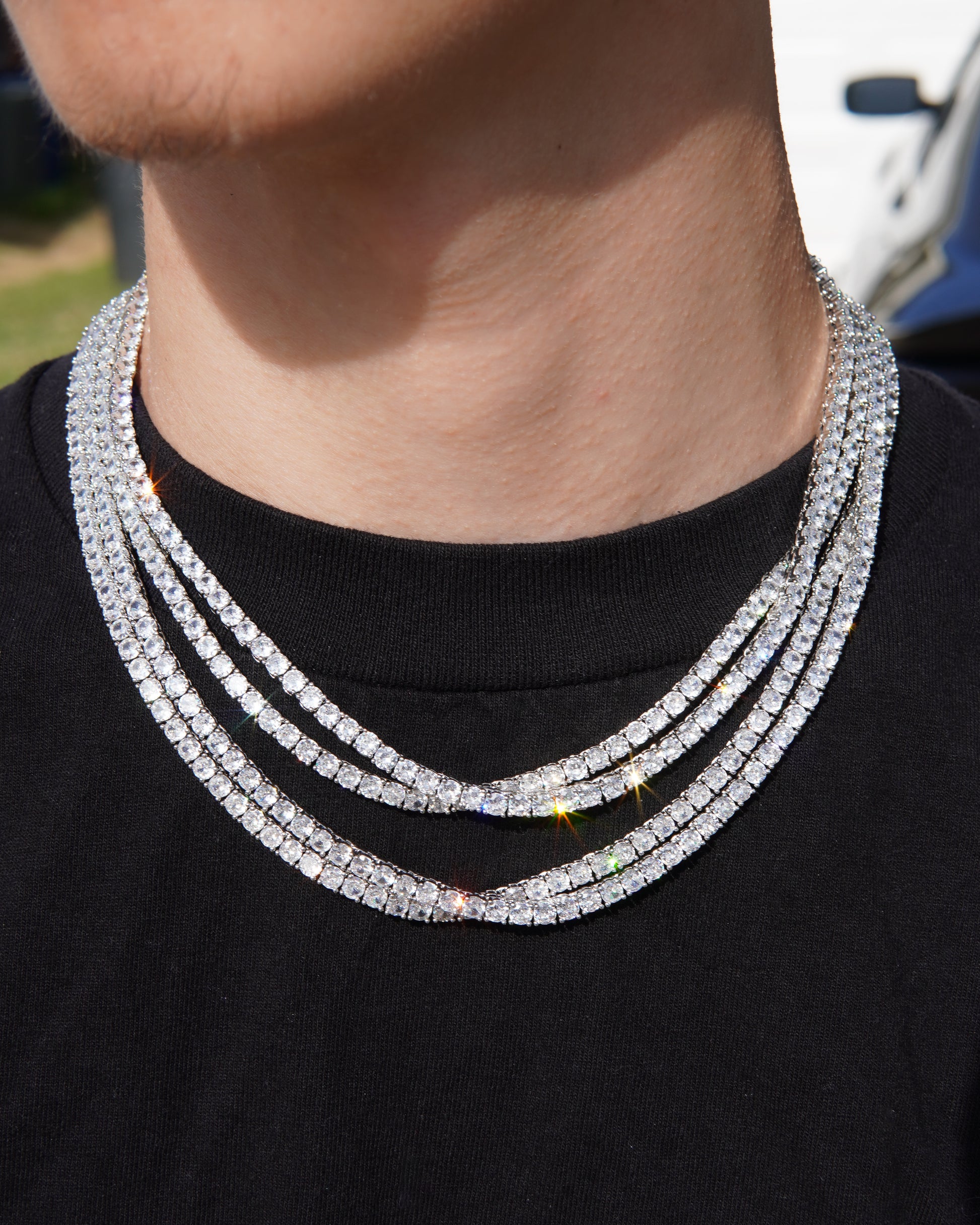Close-up of a person wearing a multiple-layered diamond necklace on a black shirt.